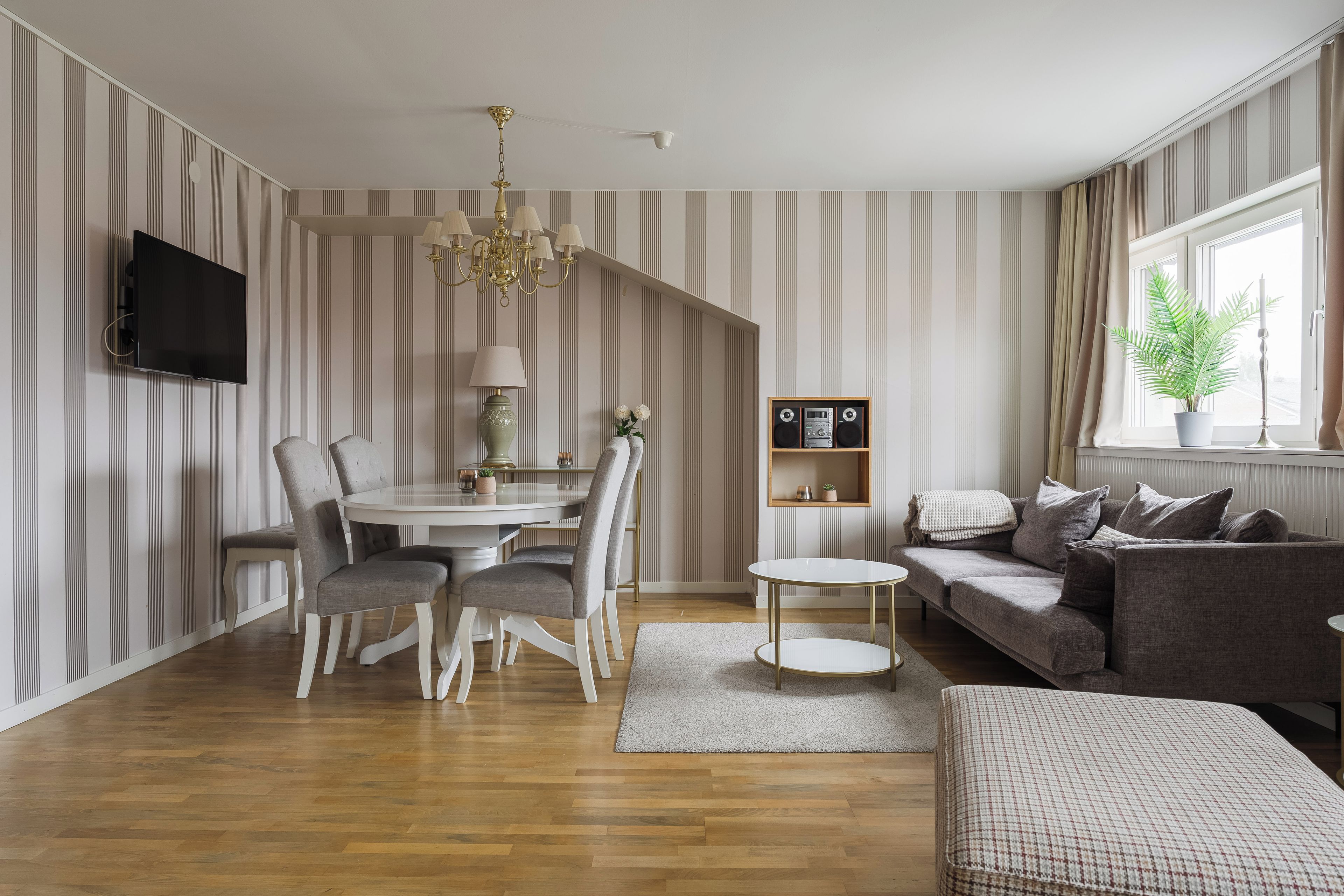 Een moderne woonkamer met een eethoek, een bank, een aan de muur bevestigde televisie en een kroonluchter.