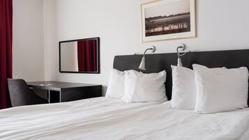 A hotel room with a bed, a desk, a chair, a mirror, and a framed picture on the wall.