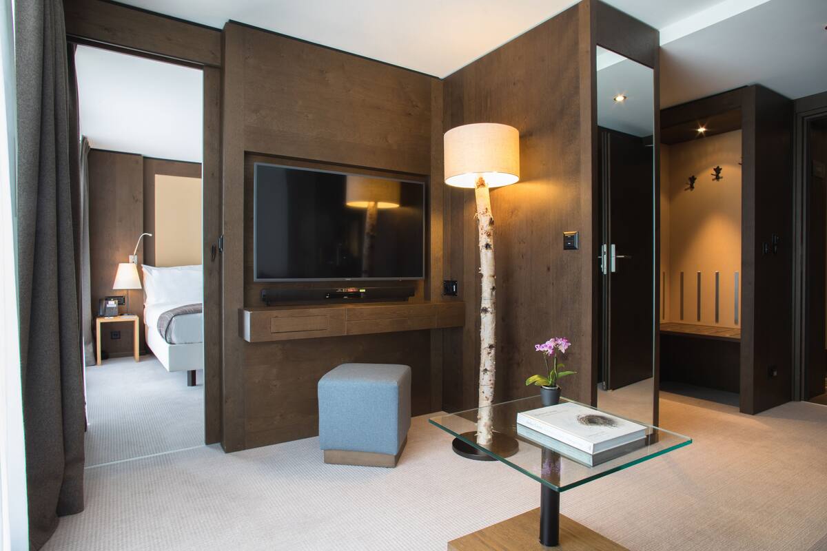 Una habitación de hotel moderna con un televisor de pantalla plana grande, una mesa de centro de vidrio, una pequeña zona de estar y una pared de acento de madera.
