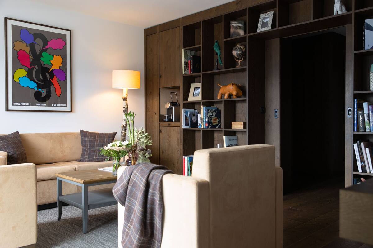 Una sala de estar con sofá, sillones, mesa de centro, estantería y lámpara.