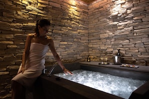 Un área de spa con pared de piedra, un jacuzzi y una mesa con una botella y copas.