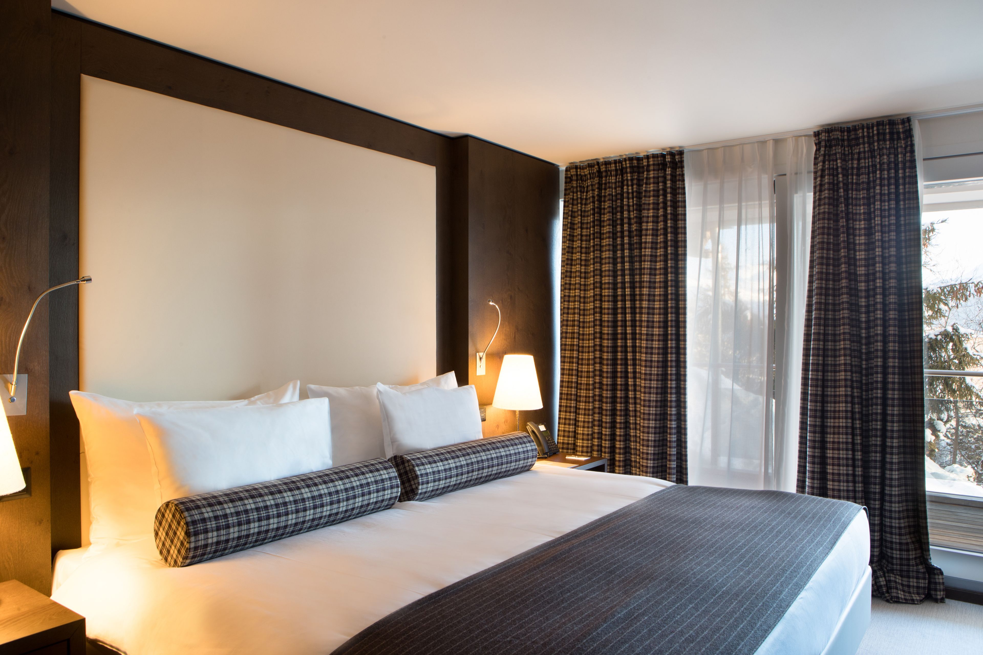 A hotel room with a large bed, a bedside table with a lamp, and a window with curtains.