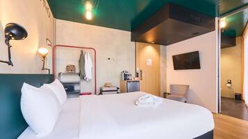 Ein Hotelzimmer mit Bett, Schreibtisch, Stuhl, Fernseher und einem durchgegangenen Tür sichtbaren Badezimmer.