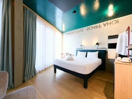 A hotel room with a bed, a desk, a chair, and a large window with curtains.