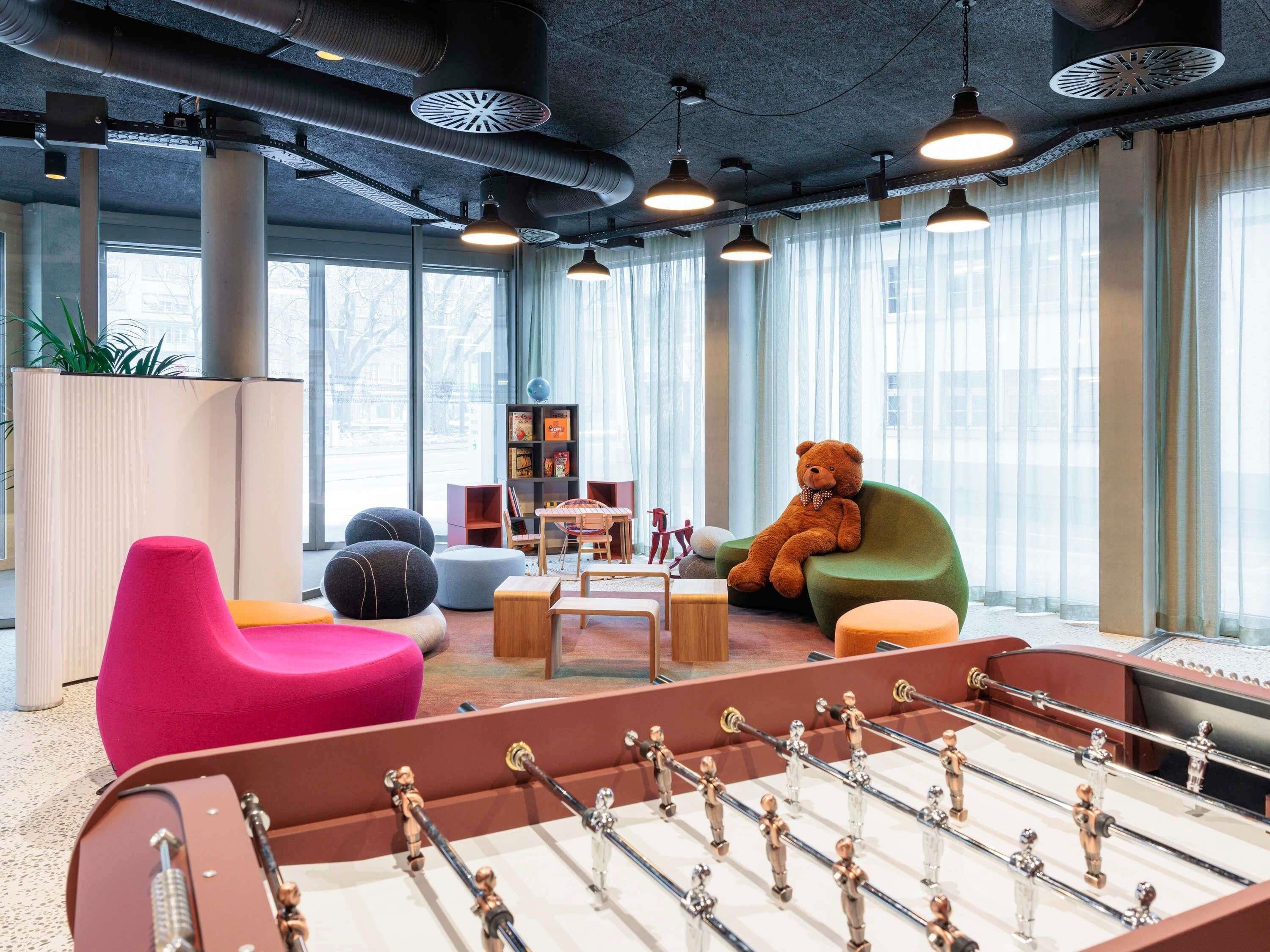 Um espaço interno moderno com mesa de futebol, assentos coloridos e grandes janelas.