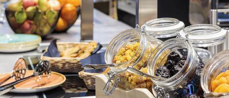 Un bufé con diferentes opciones de comida, incluyendo frutas, cereales y pastelería.