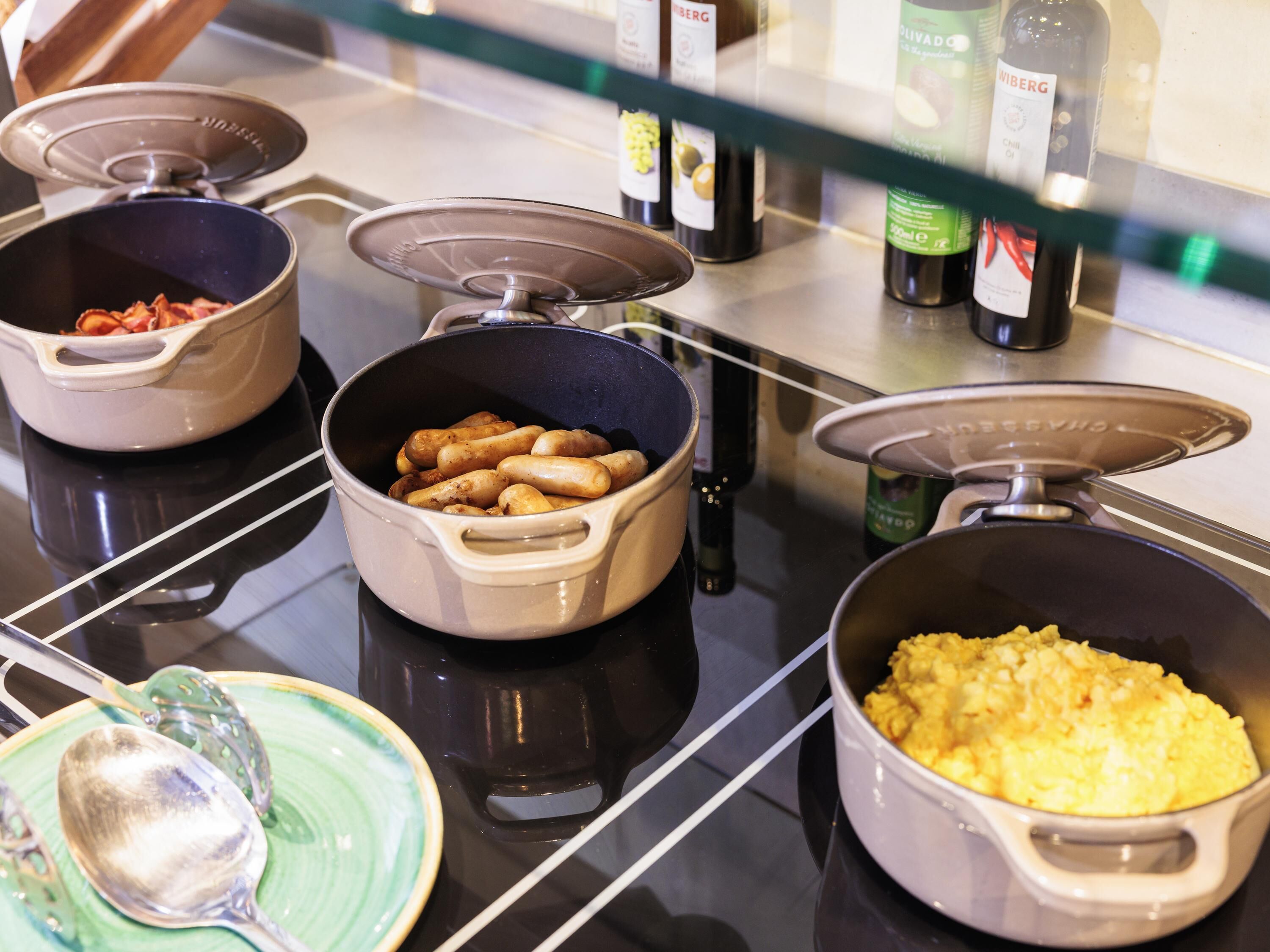 Un bufé con diversos alimentos en recipientes, una cuchara y salsas sobre una barra.