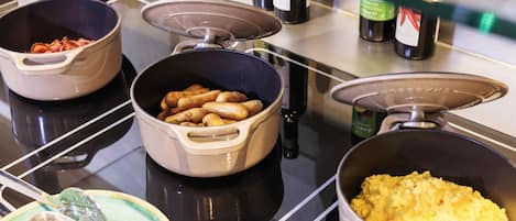 Un bufé con diversos alimentos en recipientes, una cuchara y salsas sobre una barra.
