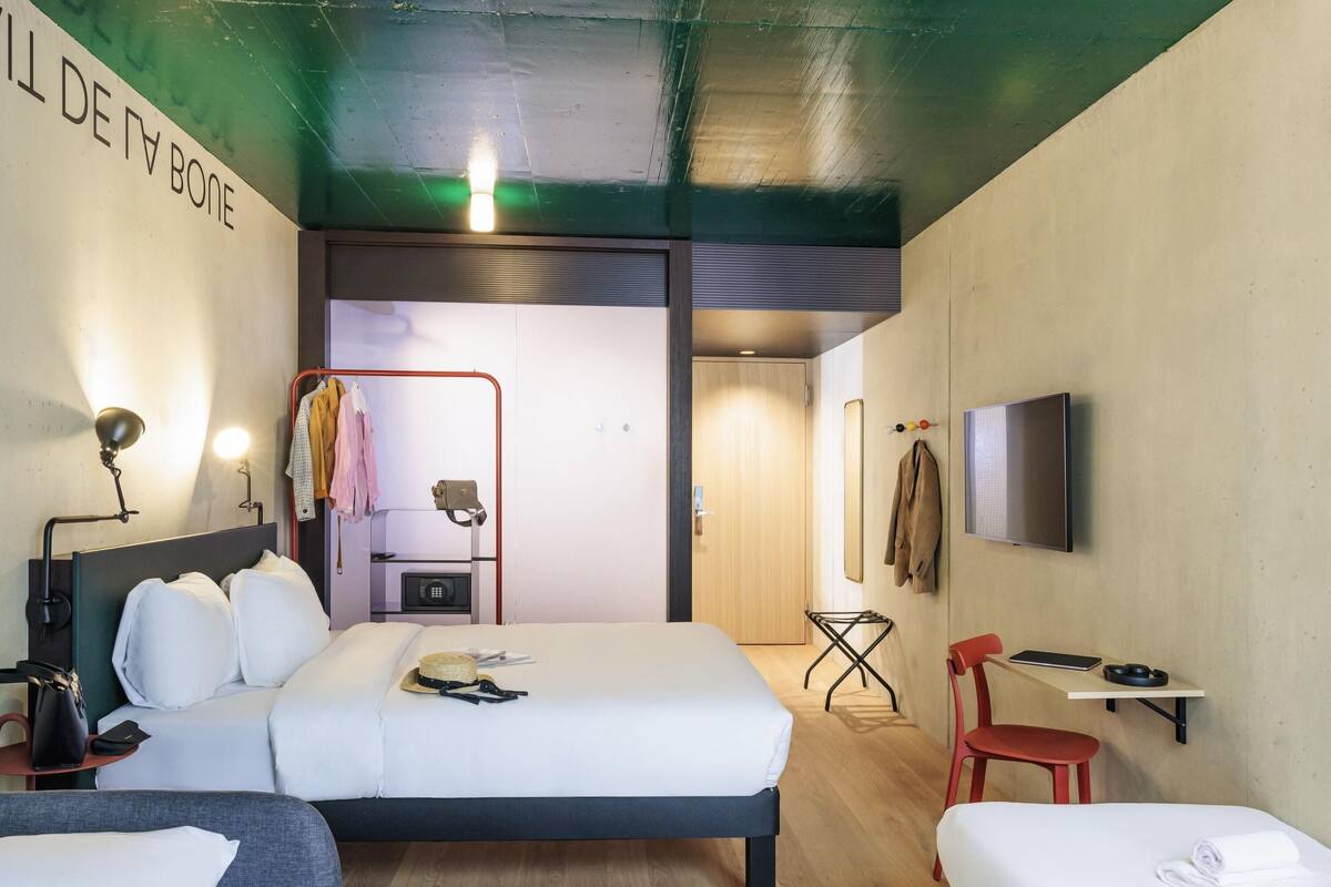 A modern hotel room with a bed, bedside tables, a TV, and a mirror.