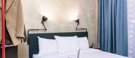 Una habitación de hotel con una cama, una computadora portátil, un abrigo colgado y una pared con un cartel.