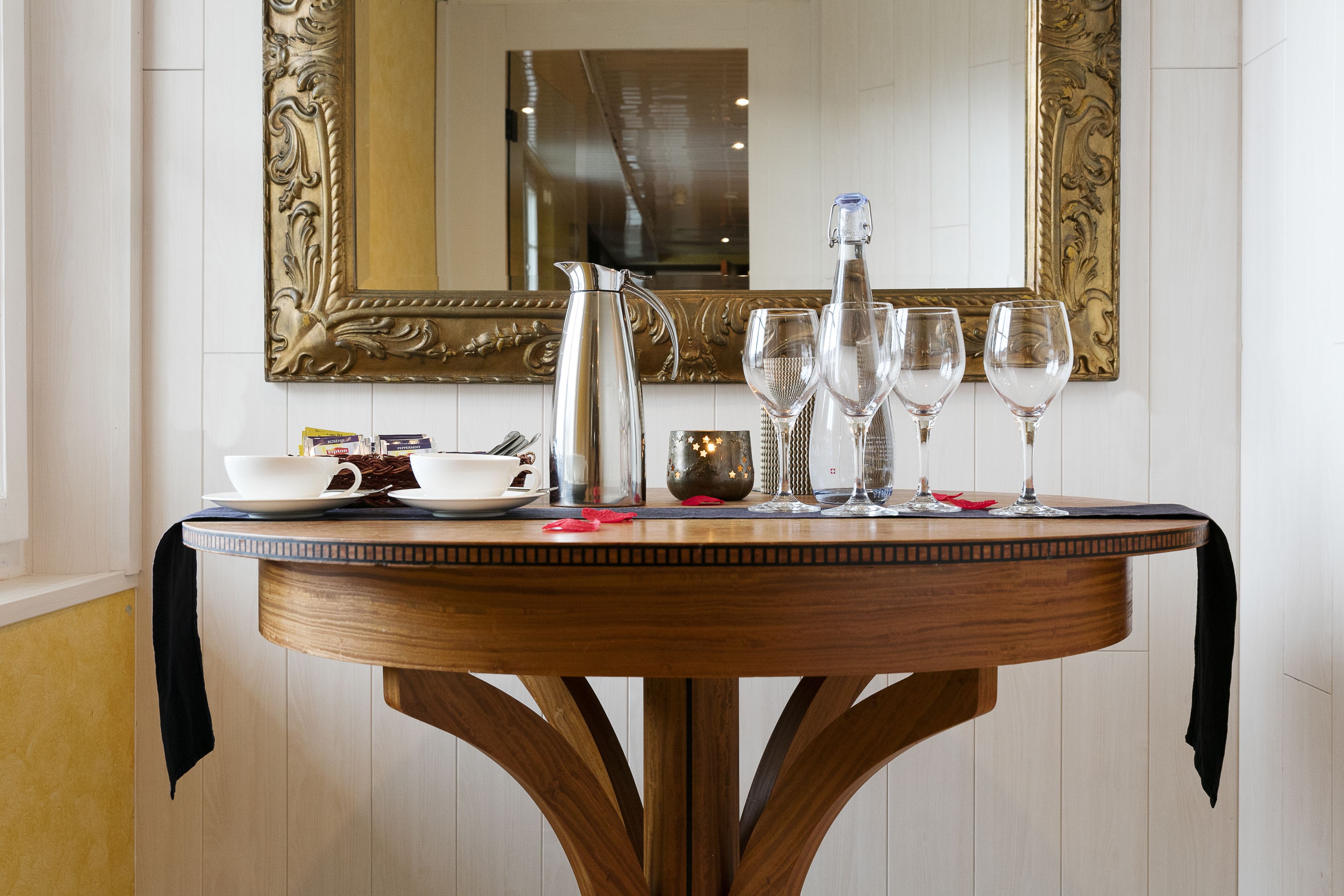 Une table ronde en bois, avec un miroir au-dessus, une carafe, deux verres et un bol de nourriture.