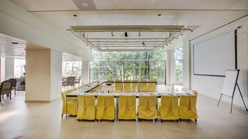 A conference room with a long table, yellow chairs, a whiteboard, and a projector screen.