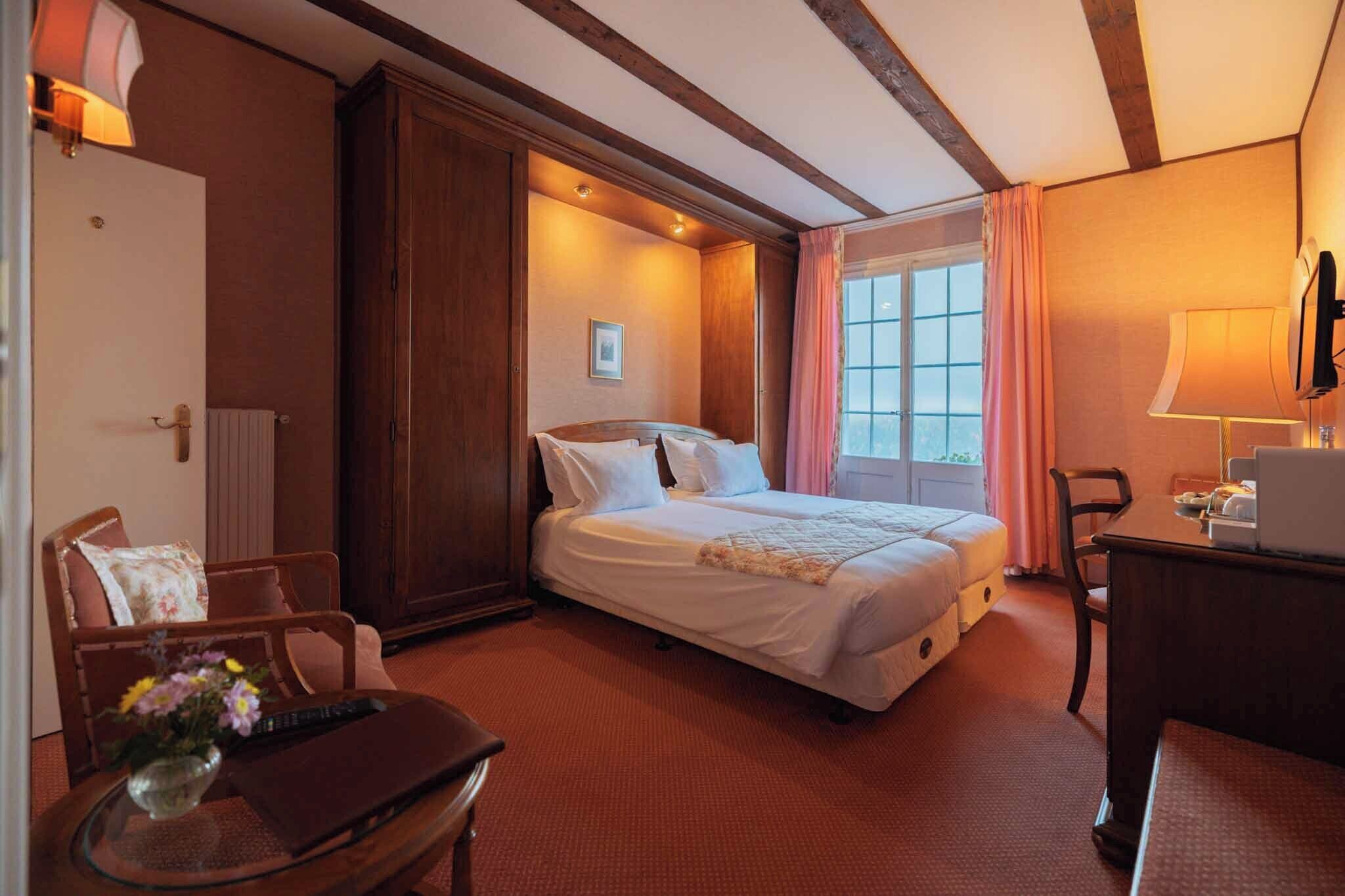 A hotel room with a bed, a desk, a chair, and a window with curtains.