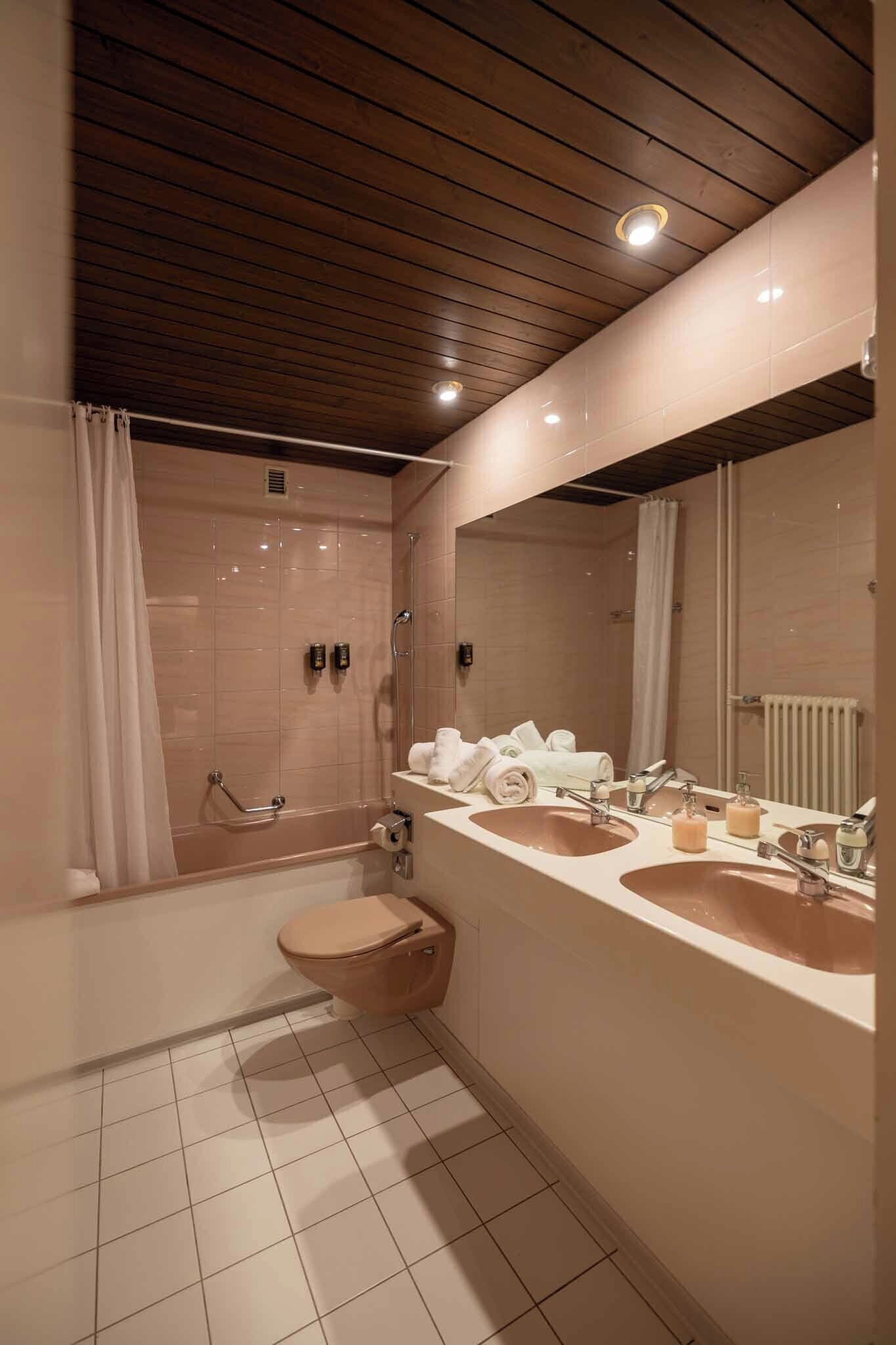 A modern bathroom with a wooden ceiling, two sinks, a toilet, and a shower area.