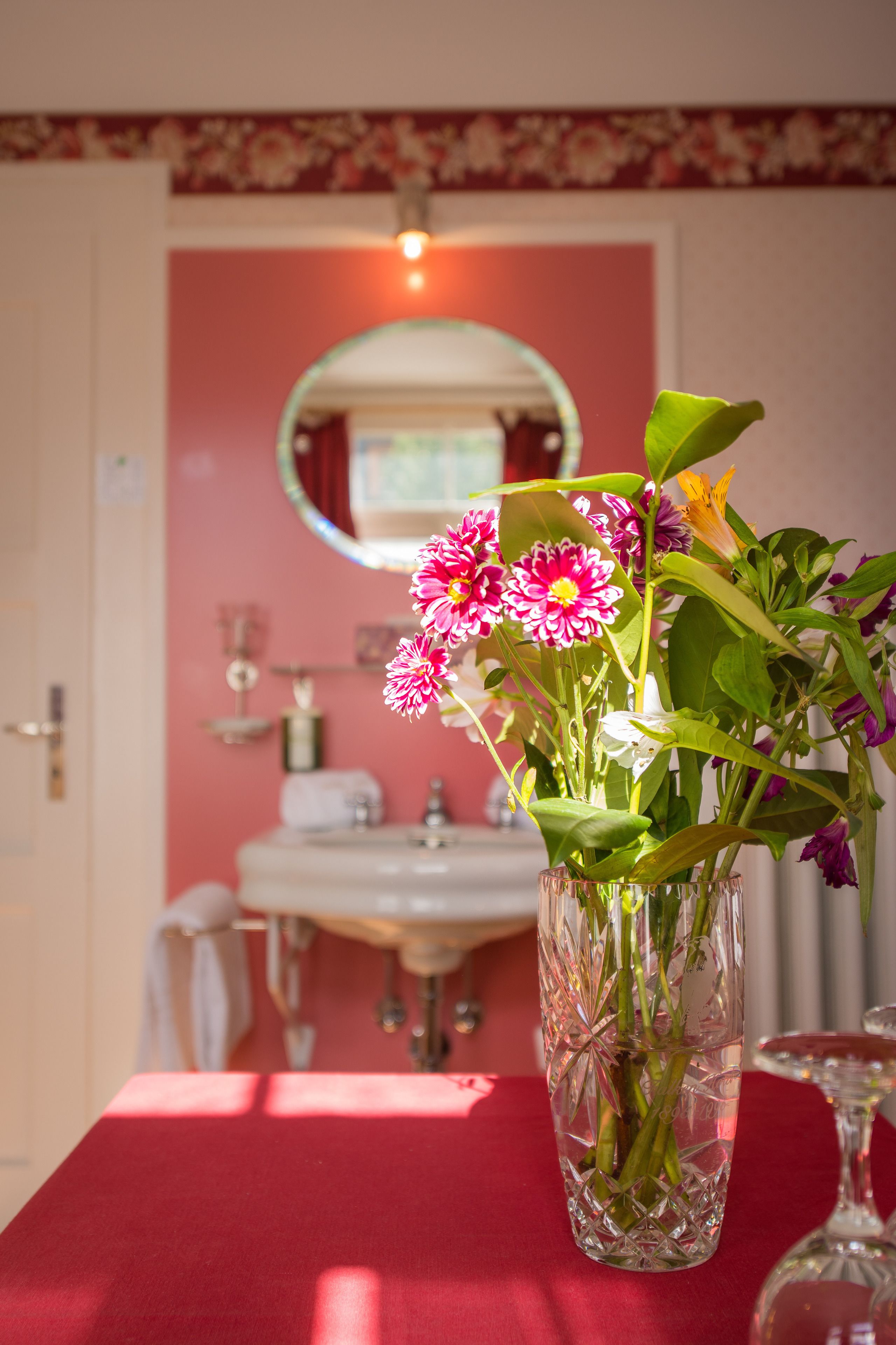 Un baño con lavamanos, espejo y un florero sobre una mesa.
