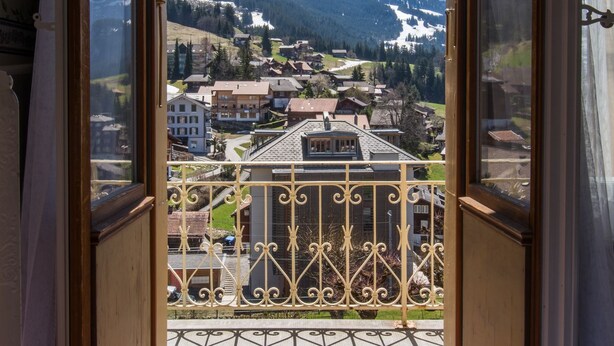 A balcony with a metal railing and a view of a snow-covered mountain and a village below. - Hotel Falken (Lauterbrunnen)