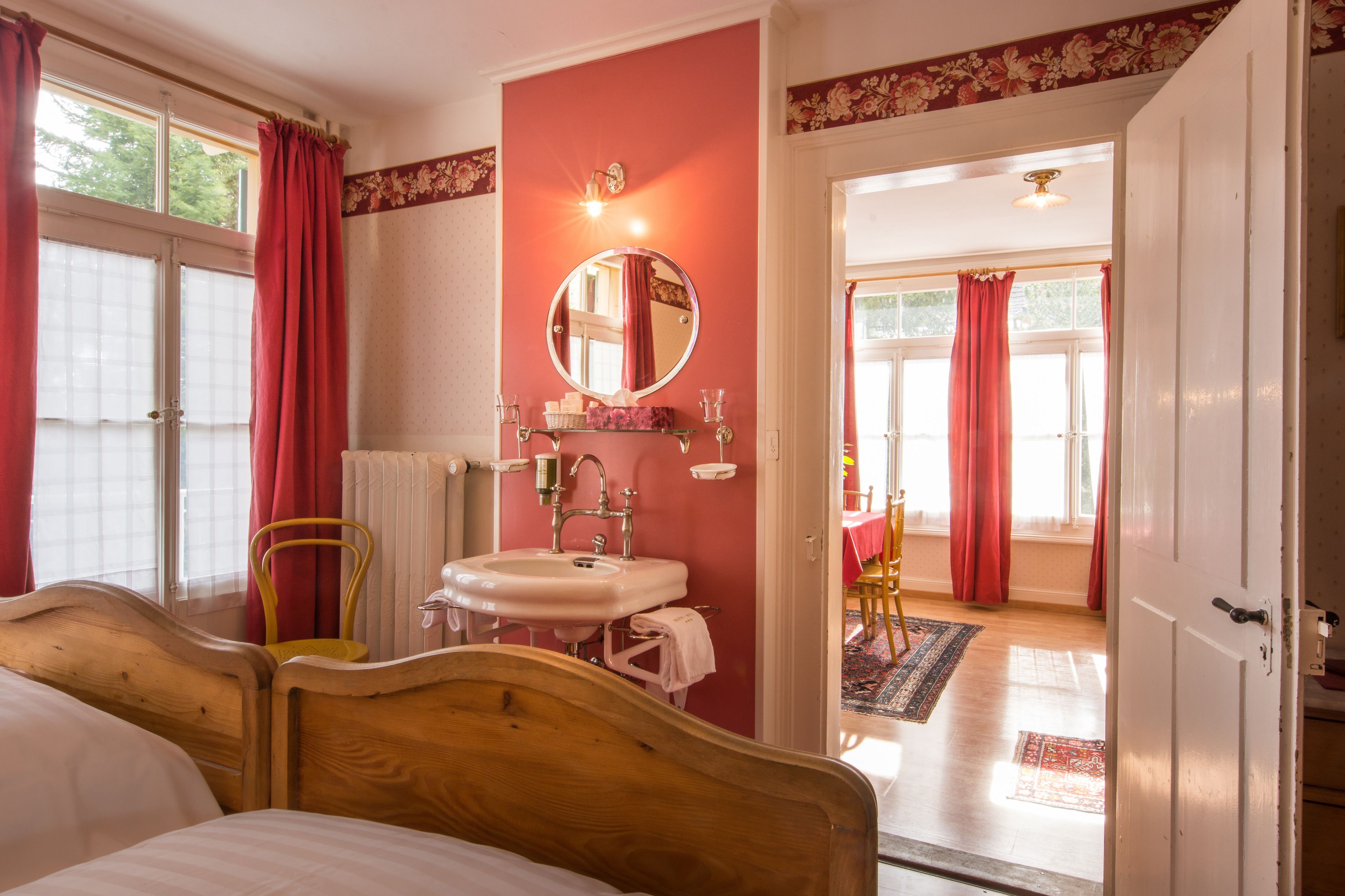 A bedroom with a wooden bed, a white sink, a mirror, and a red wall.