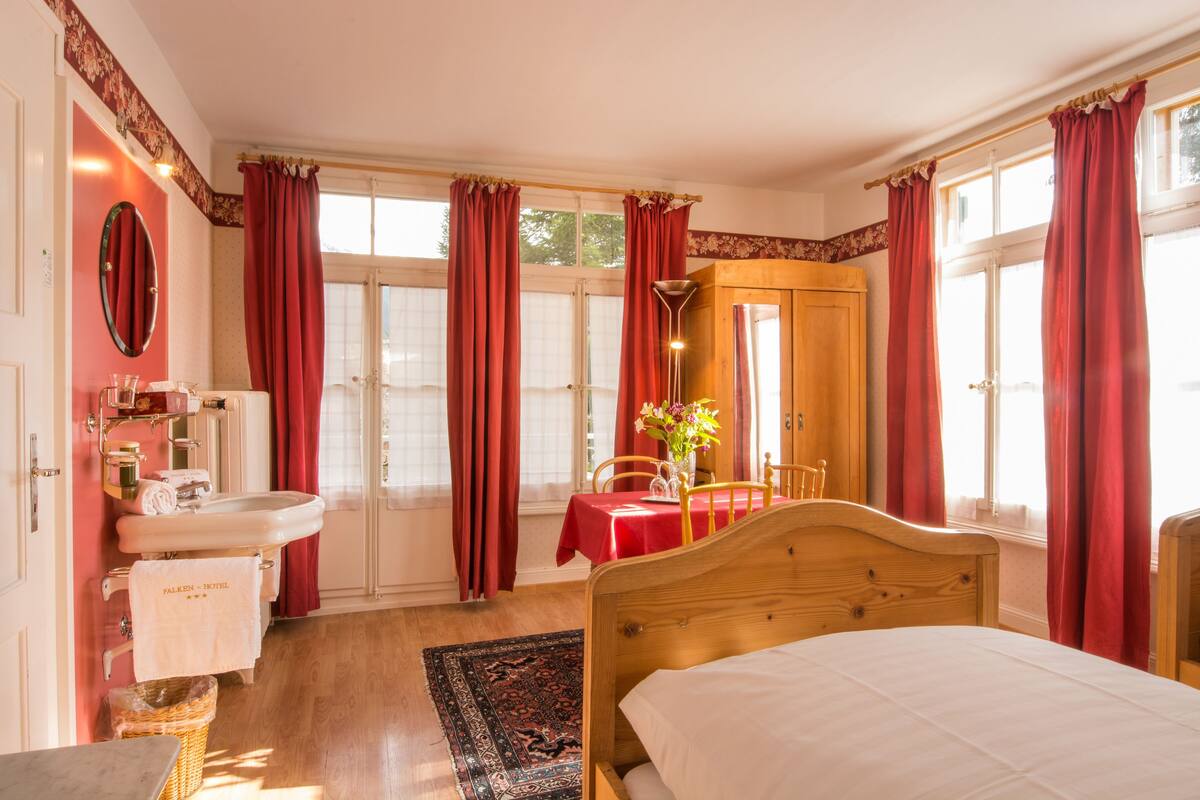 A bedroom with a wooden bed, a red table, a white sink, and a mirror.