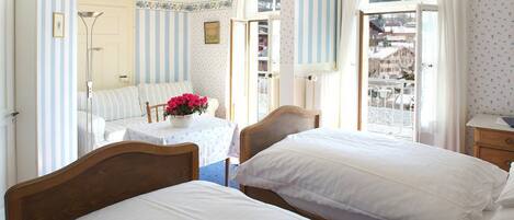 Ein Schlafzimmer mit zwei Betten, einem kleinen Tisch mit Blumenvase und einem Fenster mit Vorhängen.