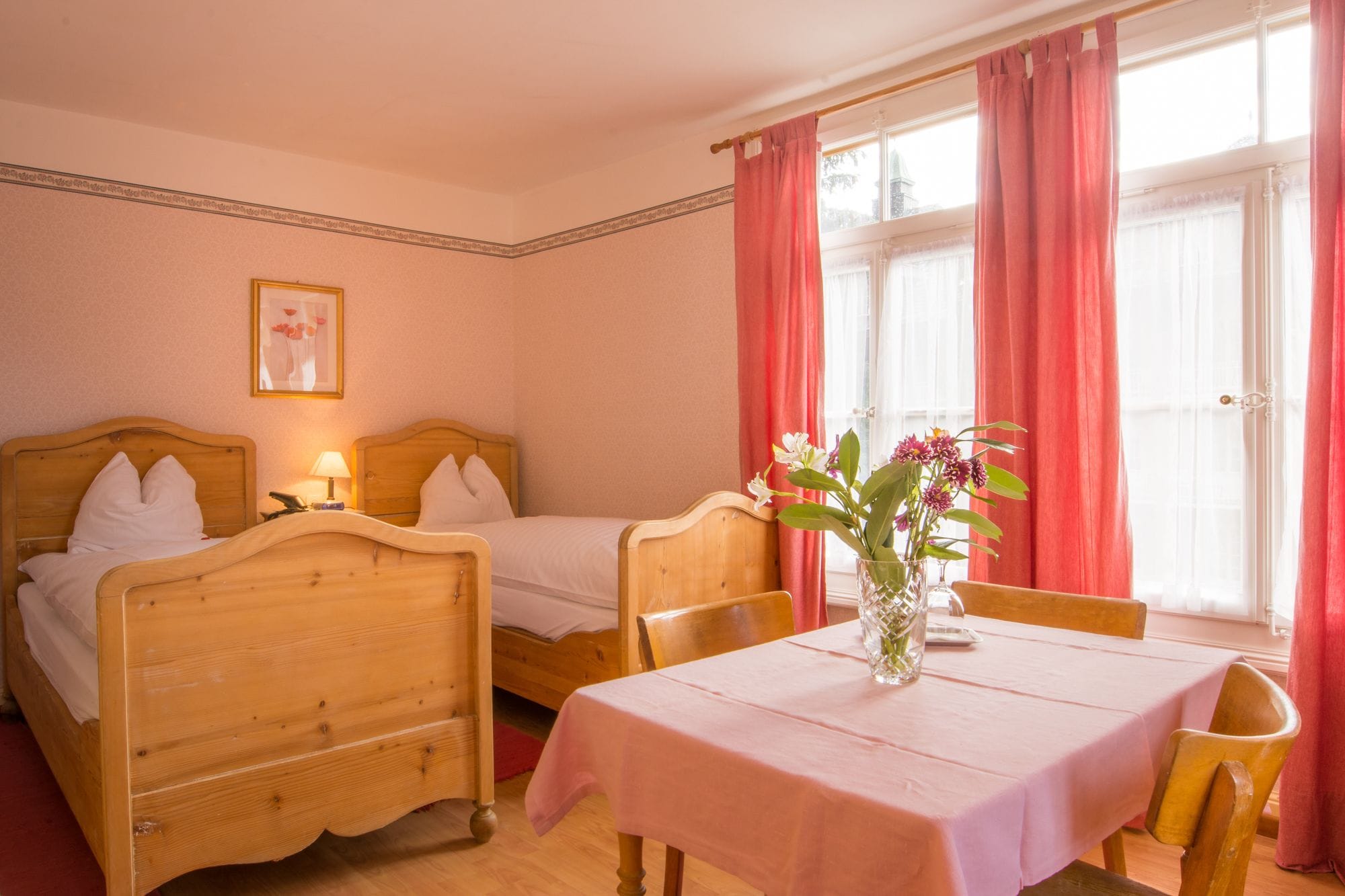 Una habitación con dos camas de madera, una mesa con mantel rosa y un jarrón con flores.