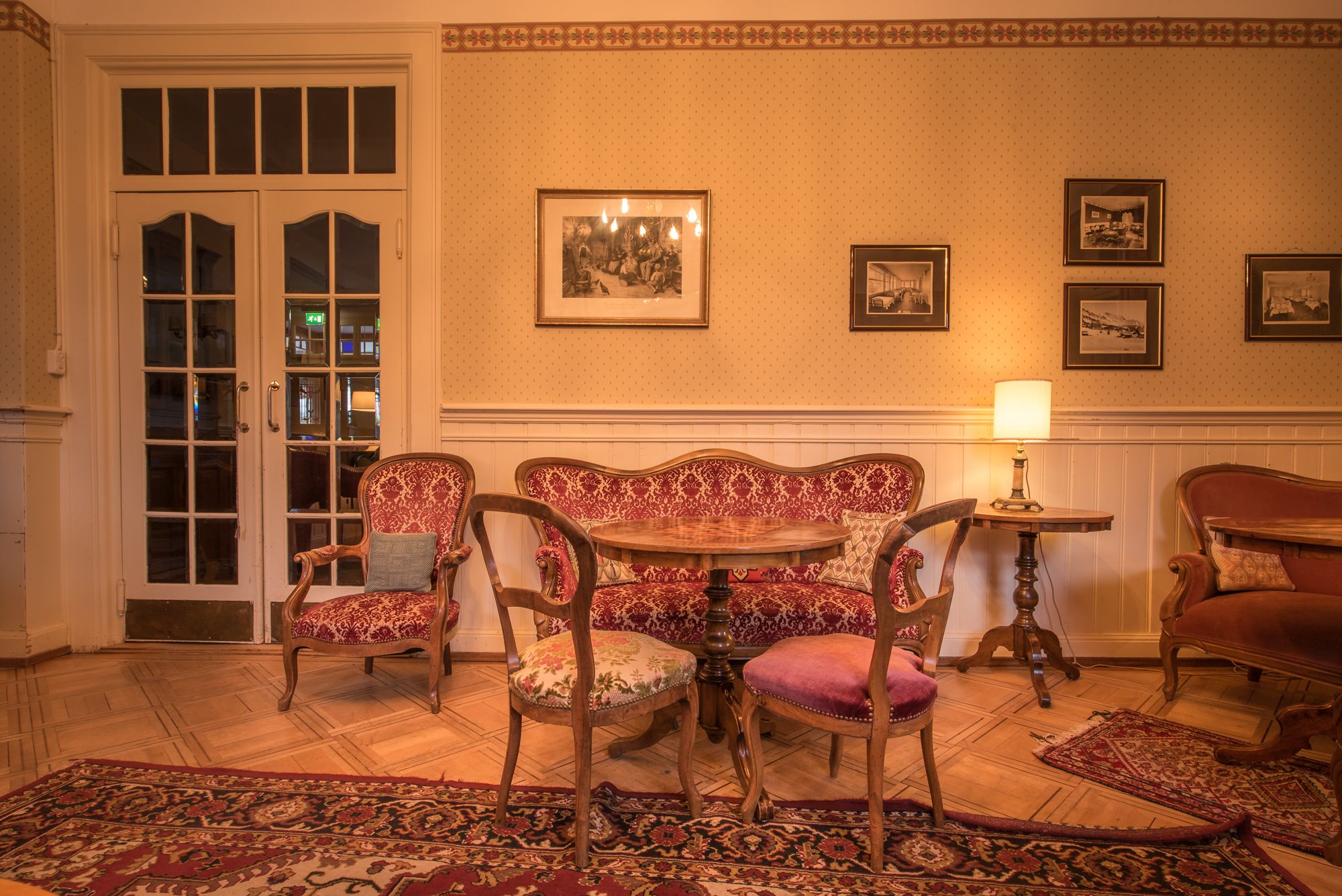 A room with a wooden table and four chairs, a patterned rug, and a door with glass panels.