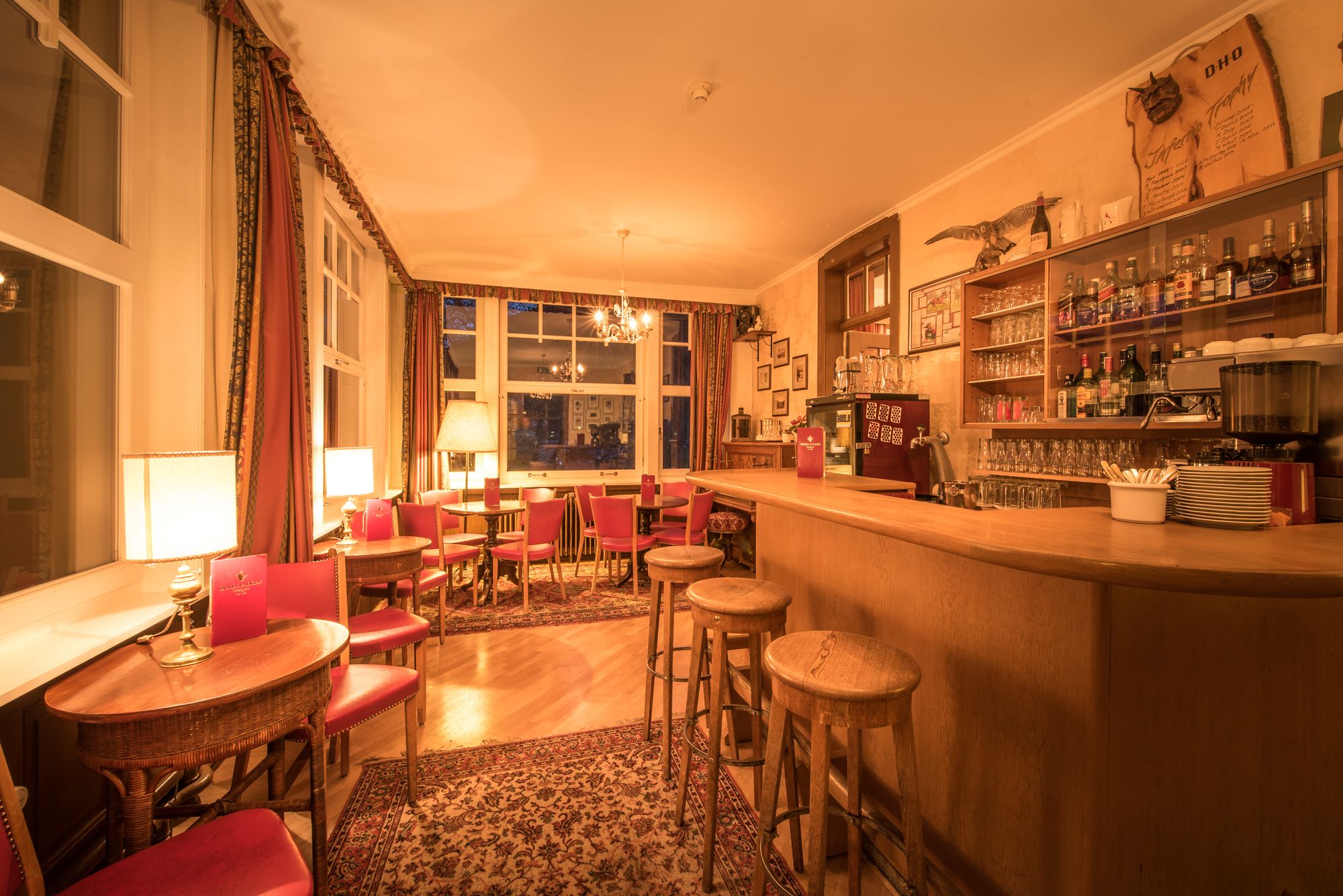 A cozy bar area with wooden furniture, a bar counter, and shelves stocked with bottles and glasses.