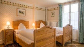 A bedroom with two wooden beds, a radiator, and a window with curtains.
