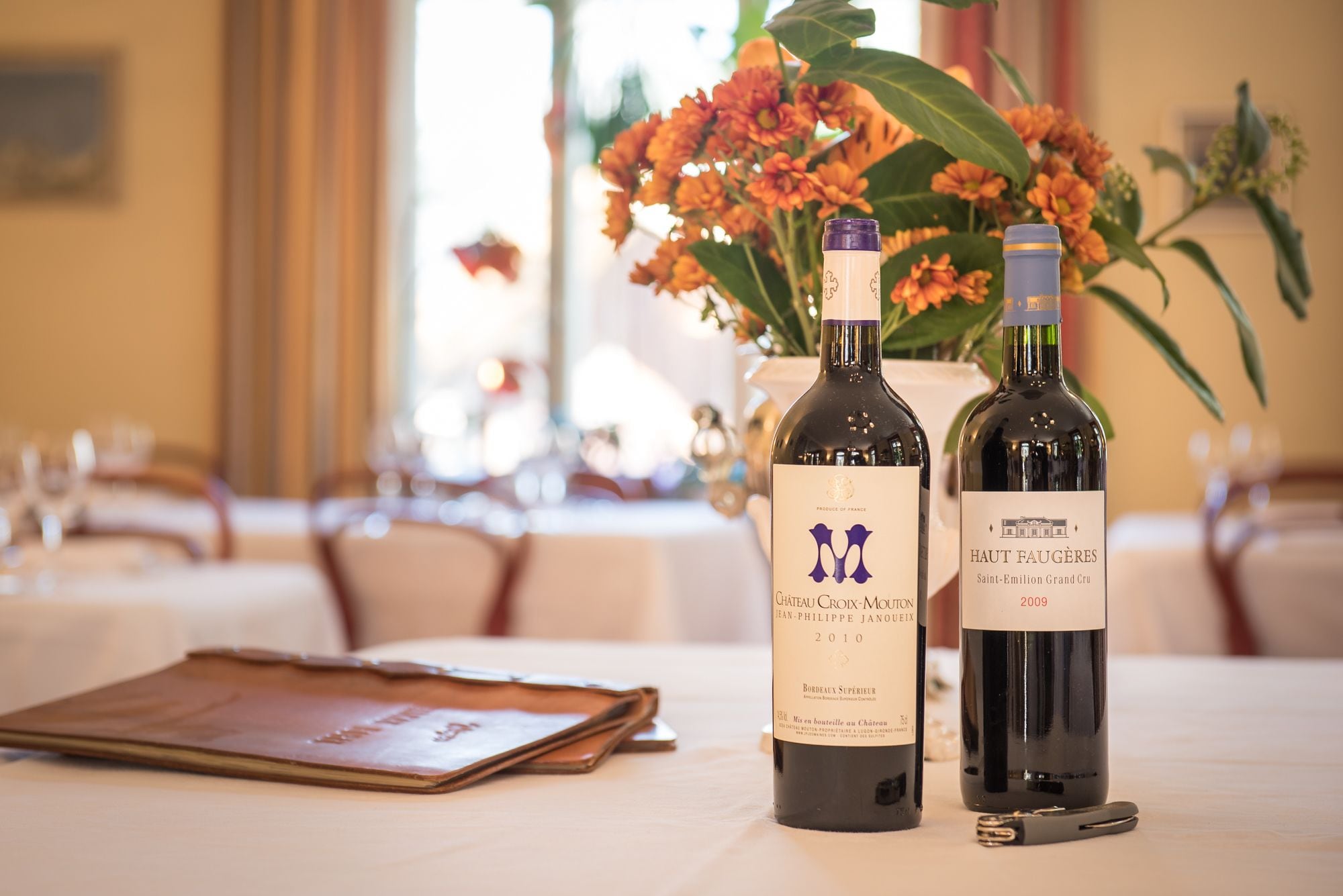 Two bottles of wine on a table with a menu and a wine opener.
