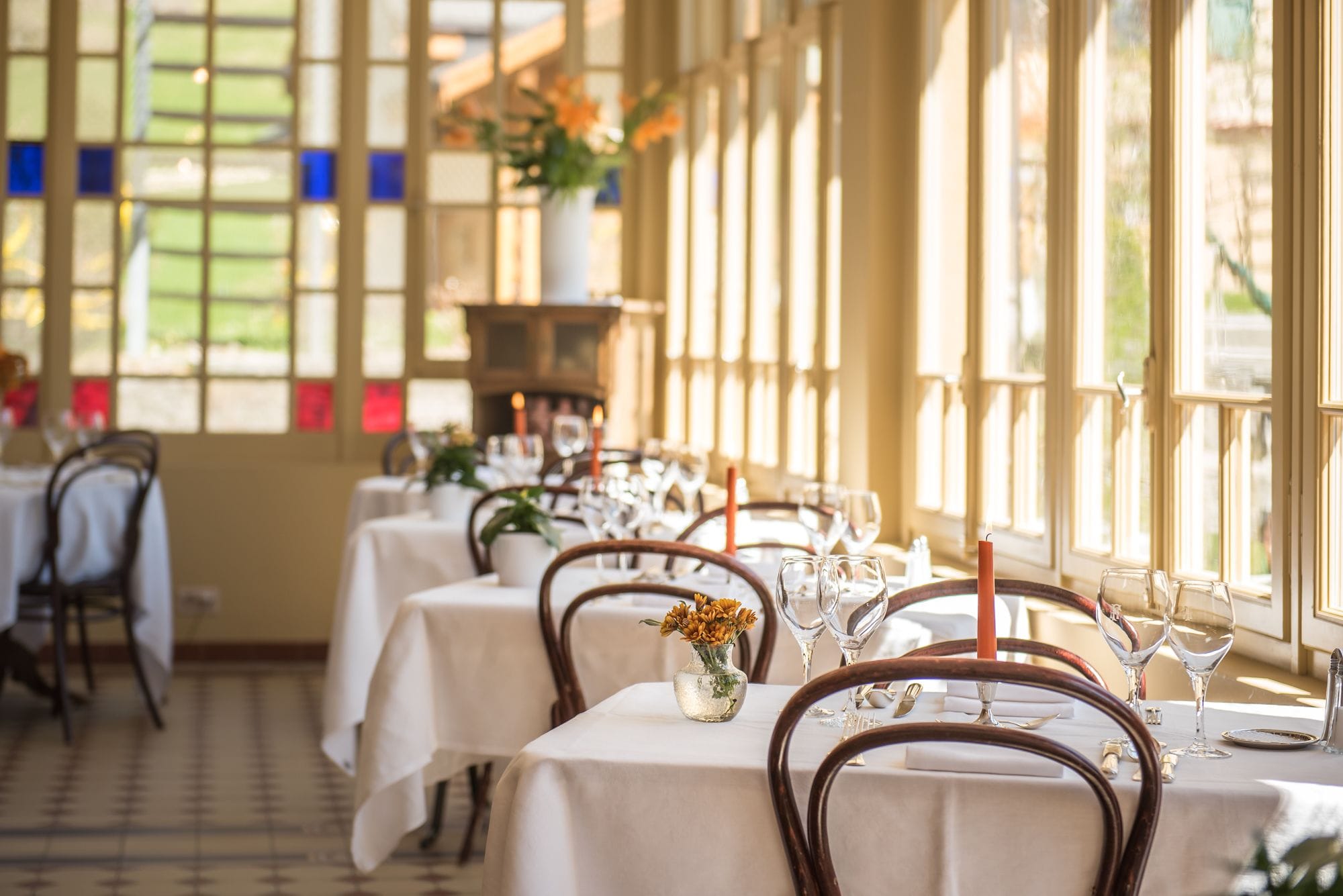 A dining area with tables set for a meal, large windows, and a view of the outdoors.