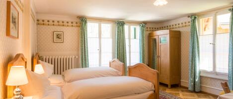 Une chambre avec deux lits, une armoire en bois, un radiateur et une table avec une lampe.