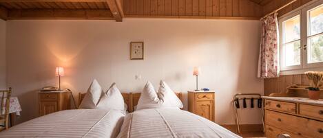 A cozy bedroom with two beds, wooden headboards, a dresser, and a window with curtains.
