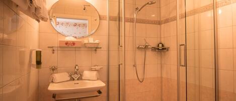 Un baño moderno con ducha de vidrio, lavamanos con espejo y perchero.