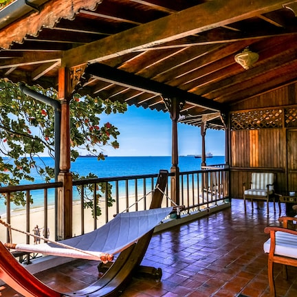 A wooden deck with a hammock, chairs, and a view of the ocean.