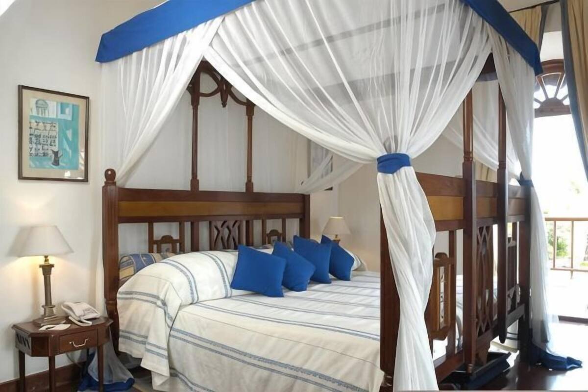 Un dormitorio con cama con dosel, lámparas de noche, una mesita de noche y un cuadro en la pared.