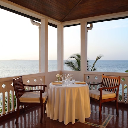 A covered outdoor seating area with a table set for two, overlooking a calm sea and a distant island.