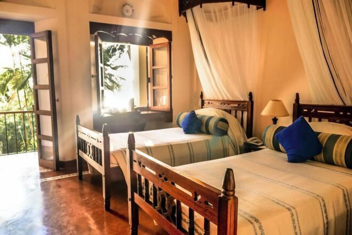 Una habitación con una cama, una mesita de noche, una lámpara y una ventana con cortinas.