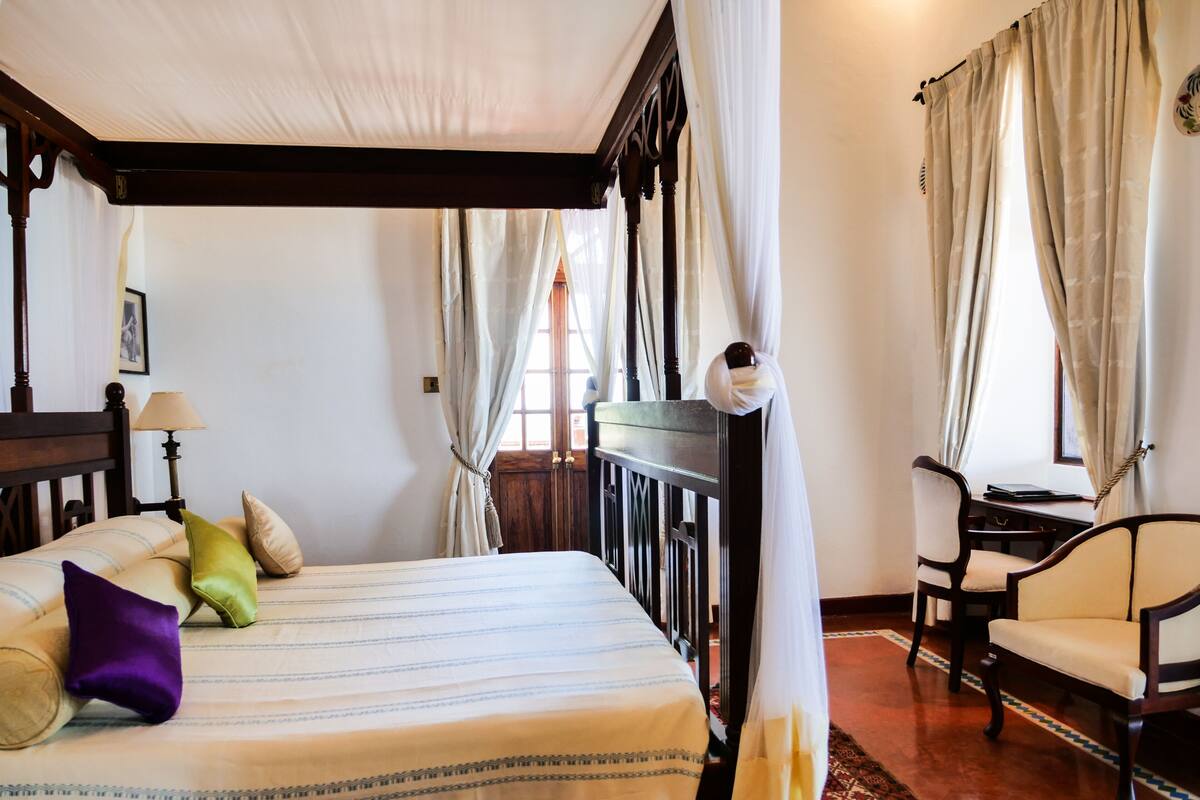 Un dormitorio con cama, escritorio, silla y ventana con cortinas.
