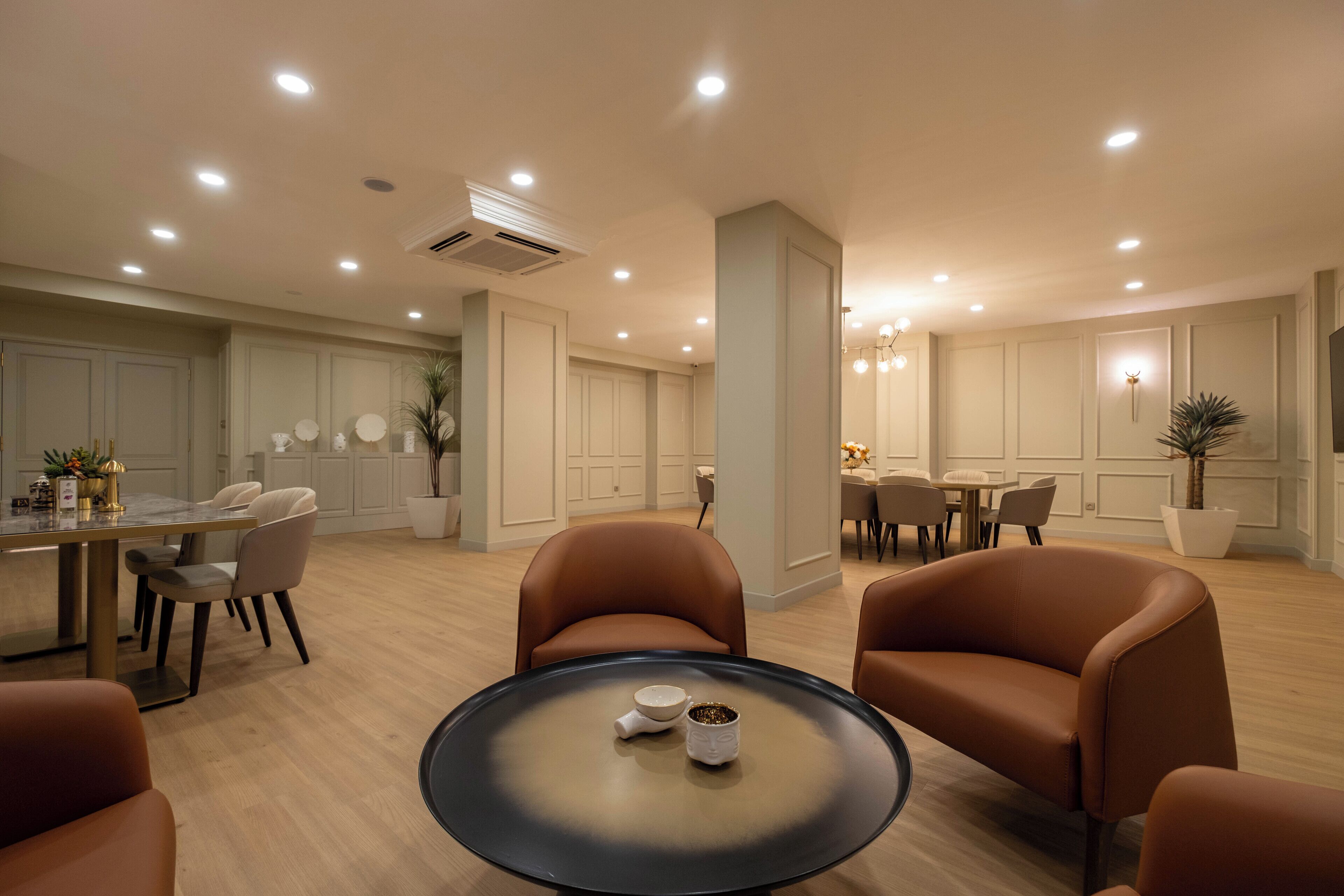 A modern hotel lobby with a dining area, seating, and a central table with a coffee pot.