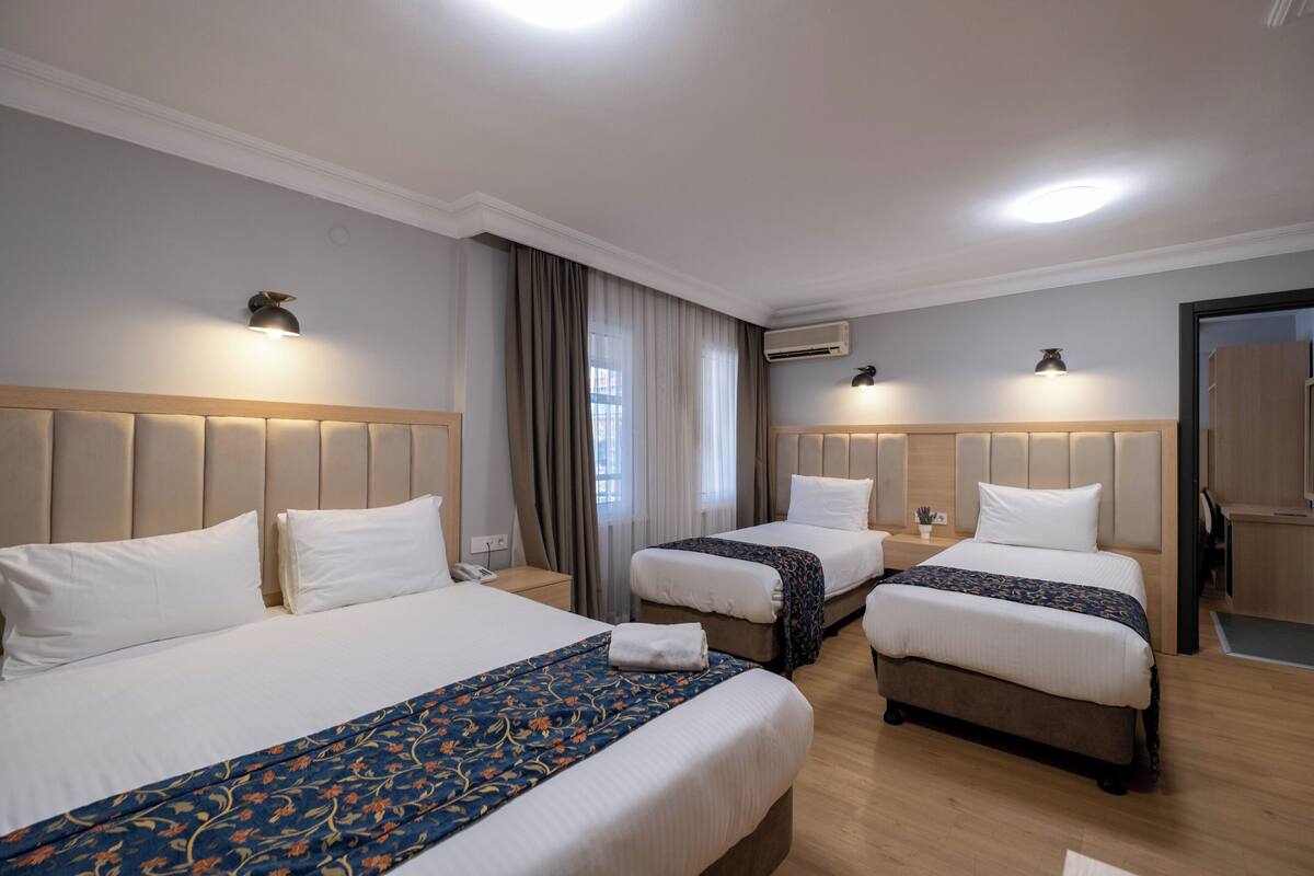 A hotel room with two beds, each with a headboard, a bedside table, and a lamp.