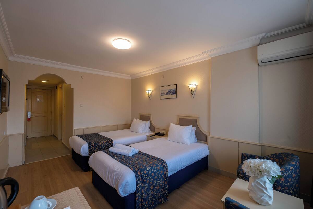 A hotel room with two beds, a small table with a vase, and a chair.