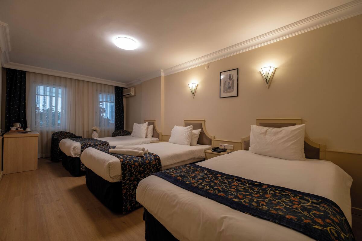 A hotel room with three beds, a desk, and a window with curtains.