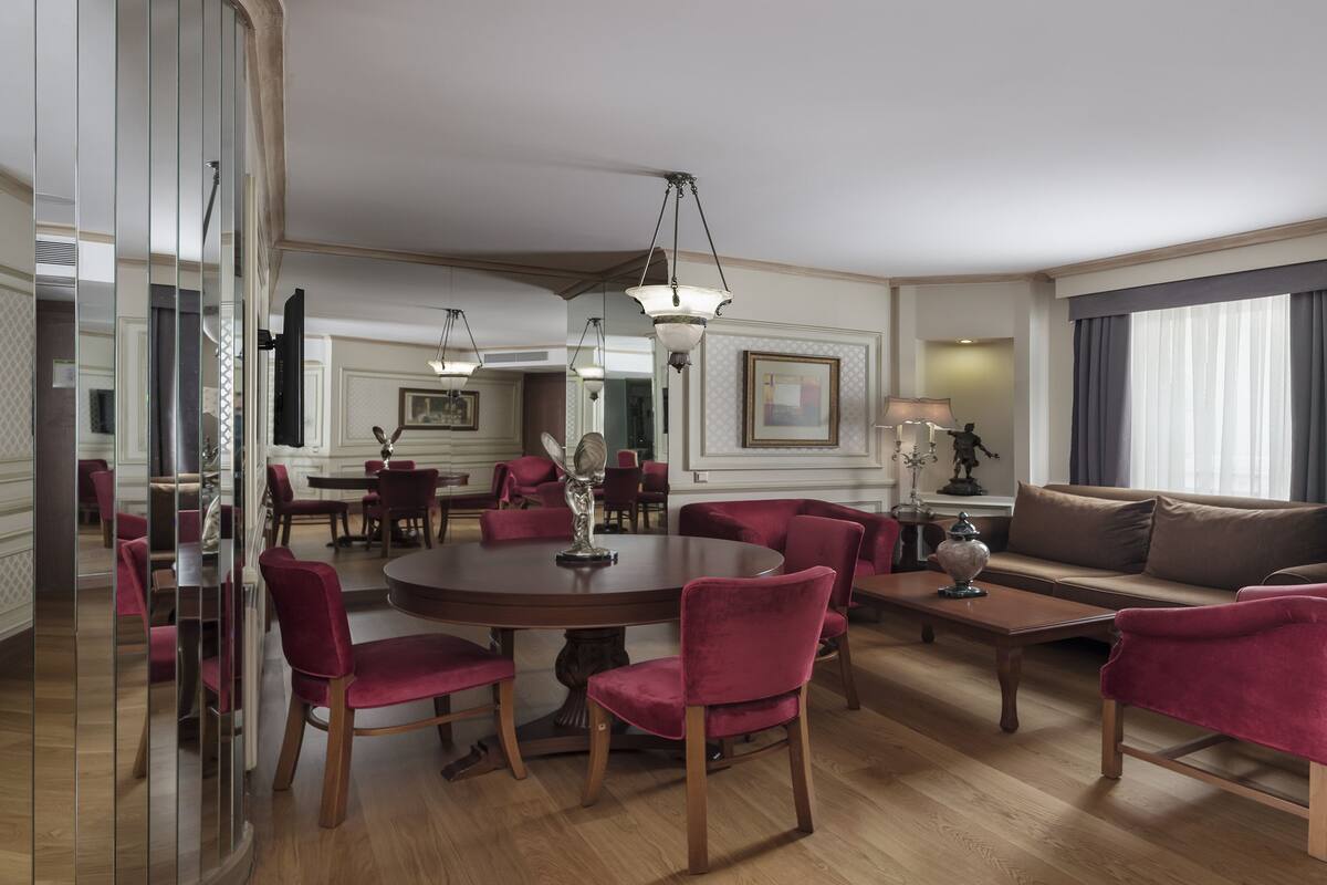 A spacious hotel room with a dining area, a sofa, and a large mirror.