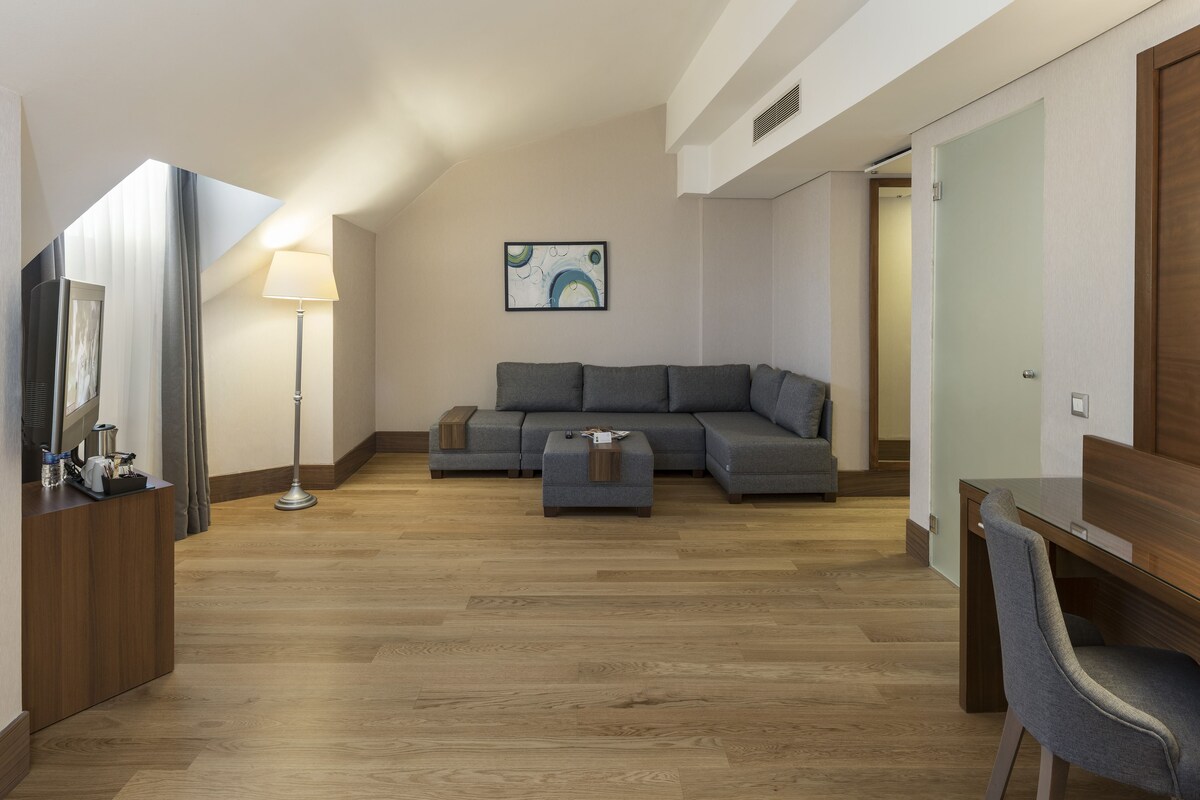 A modern living room with a sectional sofa, a small ottoman, a desk with a chair, and a floor lamp.