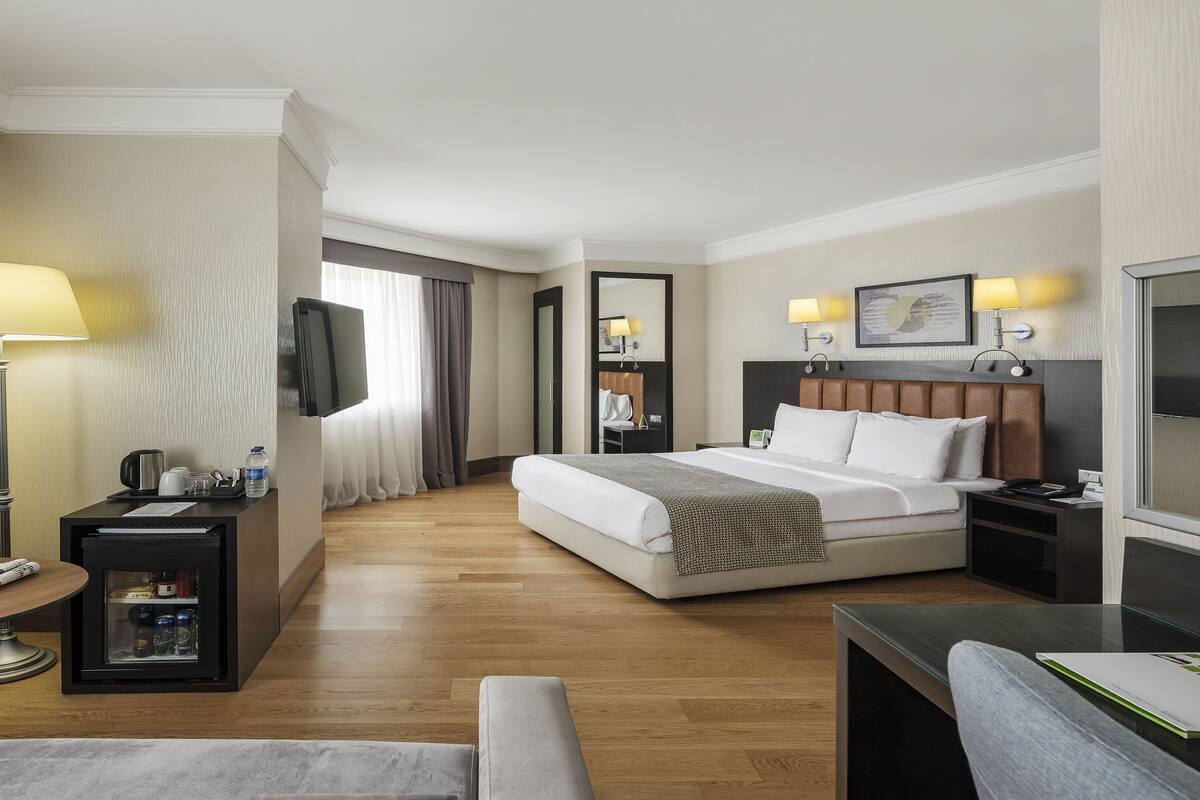A hotel room with a bed, bedside table, lamp, TV, and a desk with a chair.