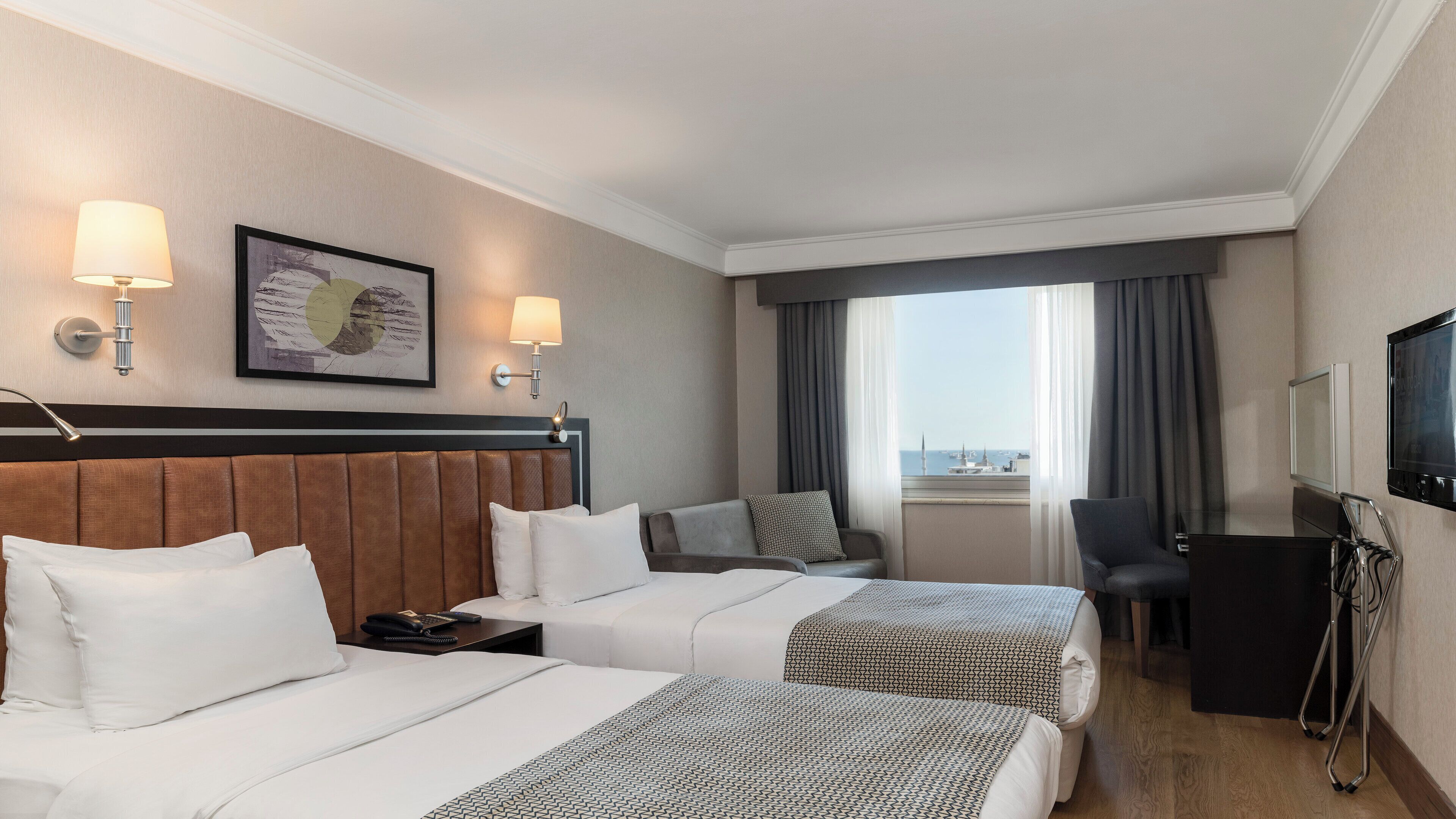 A hotel room with two beds, a desk, a chair, a TV, and a window with a view.