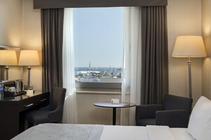 Una habitación de hotel con una cama, dos sillones, una mesita y un escritorio con lámpara y cafetera.