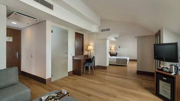 A hotel room with a wooden floor, a TV, a desk with a chair, a bed, and a sofa.