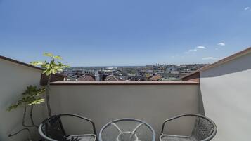 Een balkon met twee rieten stoelen en een kleine tafel, met uitzicht op een stadsgezicht met gebouwen en een heldere lucht.