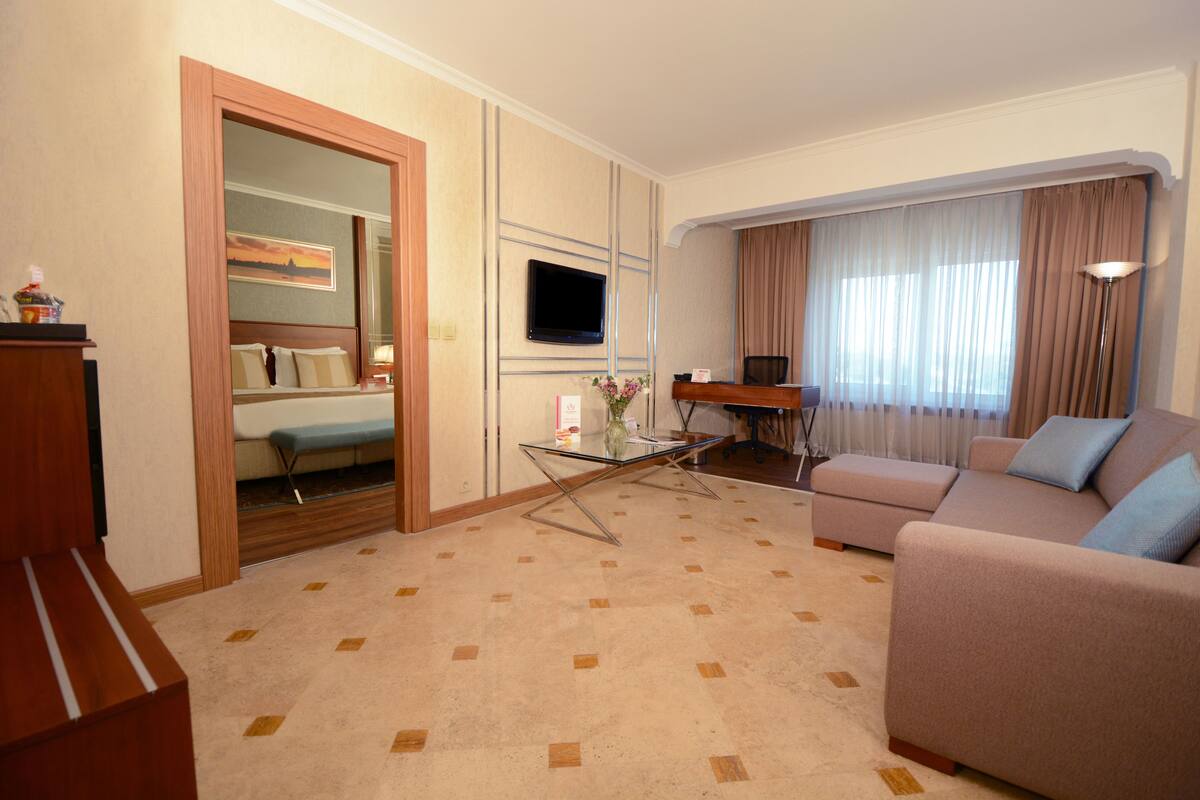 A hotel room with a bed, a sofa, a TV, a desk, and a mirror.
