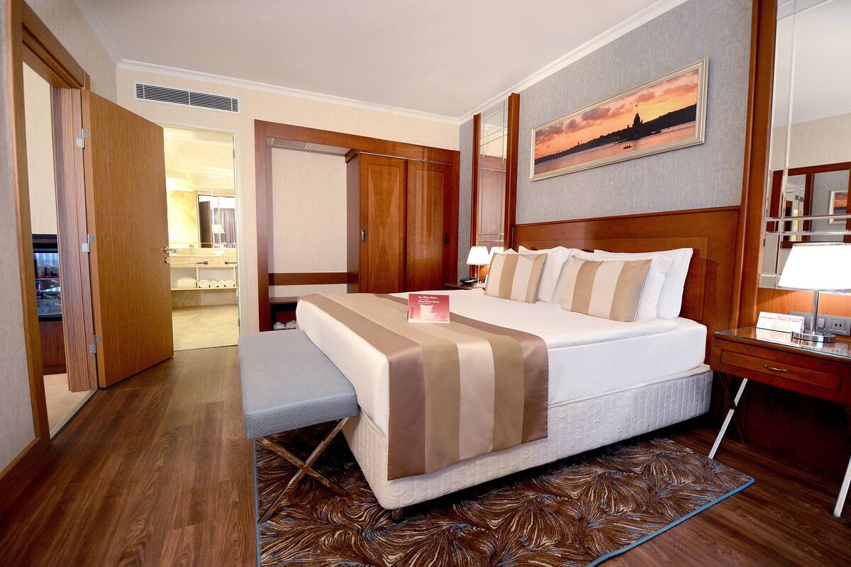 A hotel room with a bed, bedside table, lamp, and a painting on the wall.